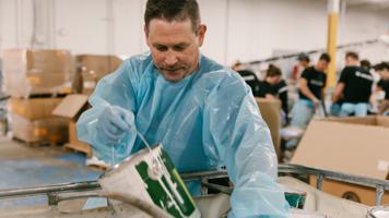 A Merus employee-owner carrying a can of paint at a service day in protective equipment