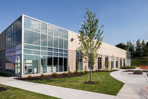 Corner view of a flex office with glass panels, beige concrete walls, and surrounding landscaped greenery
