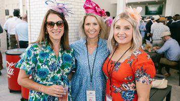 Three women dressed in colorful outfits and decorative hats posing together at an event.