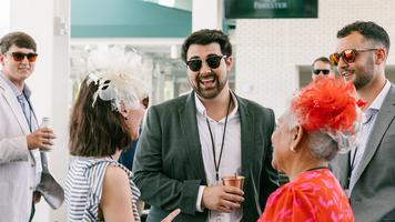 Three employee-owners dressed in colorful outfits and decorative hats talking together at an event.