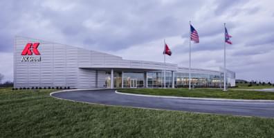 AK Steel building with a modern facade, three flagpoles, and a curved driveway surrounded by grass.