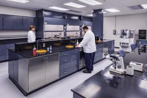 Laboratory with scientists in white coats working at counters, surrounded by equipment and microscopes.