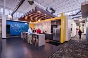 Modern office kitchenette with a seating area, bright yellow accents, and motivational wall text.