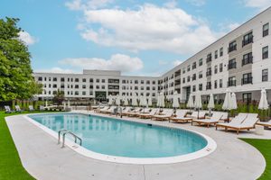 Pool shown with white chairs behind white and gray building