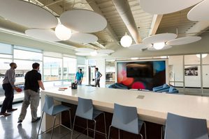 Modern office space with a large table, colorful seating, and employees playing ping-pong.