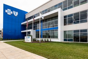 Exterior of Anthem office building with glass walls, a blue facade, flagpoles, and a landscaped lawn. The Anthem logo is located on blue accent wall