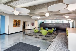 Office lounge with green chairs, modern decor, and a wall sign reading Solutions for a healthier future.