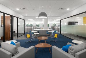 Modern office lounge with gray seating, blue accents, and glass-enclosed meeting rooms.