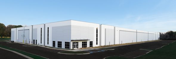 Concrete industrial warehouse with white exterior and a glass entrance.