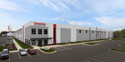 A gray and white industrial building with red signage and cars in the parking lot.