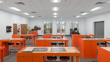 Inside of industrial building with orange desks and black stools.