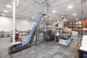 Interior of the Cancer Diagnostics facility featuring advanced machinery, including a large conveyor system and packaging equipment. The space is clean, well-organized, and illuminated by bright overhead lighting.