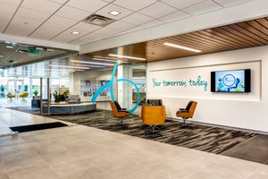 Modern office lobby with yellow chairs, motivational wall text saying Your Tomorrow, Today, and glass entry to open workspace.