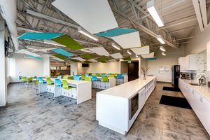 Bright office breakroom with colorful ceiling panels, high-top seating, and a kitchenette.