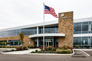 Office building with stone accents, glass facade, landscaped entrance, and an American flag flying on pole in front of building.