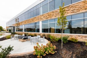 Office building with stone and glass facade, outdoor seating area, and landscaped surroundings.