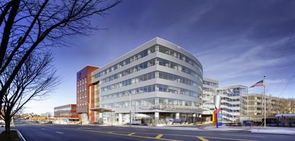 Medical office building with curved glass facade and red accent wall in urban setting.