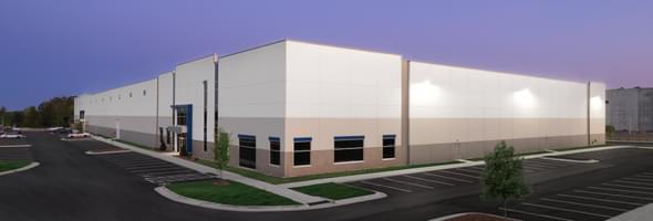 Industrial warehouse with white facade, large windows, and empty parking lot at dusk.