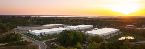 Aerial view of an industrial park with multiple white buildings and one under construction, with a sunset in the background.
