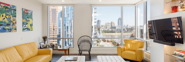Living room with yellow furniture, colorful art on the walls, large windows, and city skyline views.