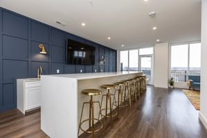 Interior tenant lounge with navy accent wall, white countertop, gold bar stools, and large windows overlooking city.