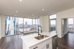 Bright modern apartment with white kitchen island, wood floors, and large windows offering city and river views.