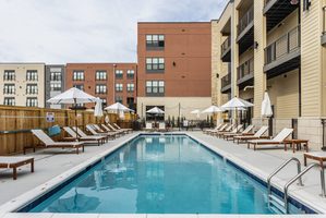 Outdoor pool area with lounge chairs, umbrellas, and surrounding apartment views.