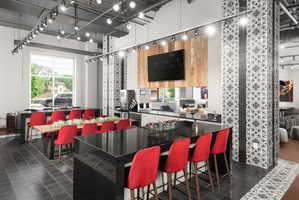 Modern communal dining area featuring red chairs, a large TV, and stylish tile accents.