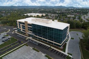 Aerial view of a modern office building with large glass windows, stone accents, and a parking lot.