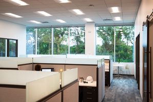 Office cubicle area with desks and partition walls in a shared workspace environment.