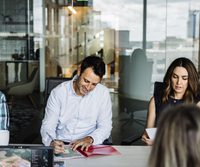 People collaborating in a modern office, seated around a glass-walled conference table