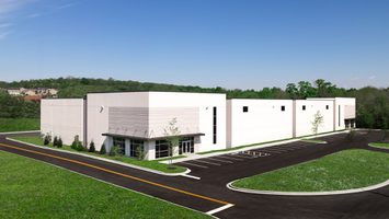 Exterior of white and gray industrial building with parking lot and landscaped surroundings.
