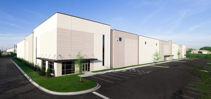 Exterior of white and gray industrial building with parking lot and landscaped surroundings.