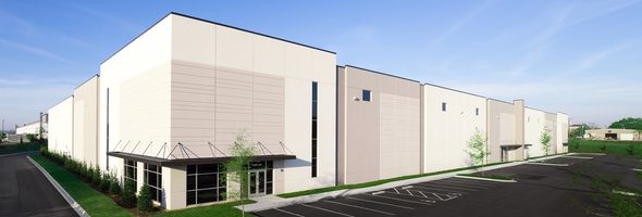 Exterior of white and gray industrial building with parking lot and landscaped surroundings.