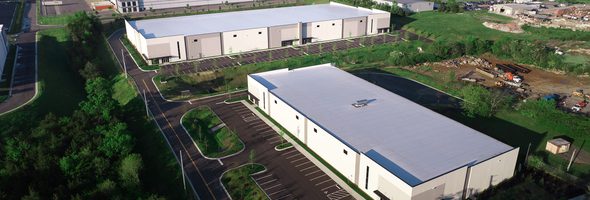 Aerial view of two white warehouse buildings with parking lots, greenery, and surrounding roads.