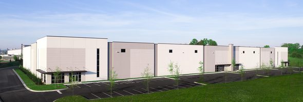 Exterior of white and gray industrial building with parking lot and landscaped surroundings.