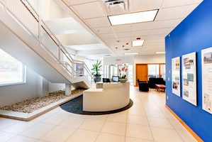 Office lobby with a reception desk, blue accent wall, staircase, and natural light.
