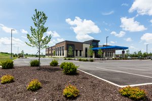 Wide view of health building with brick facade, blue canopy, and landscaped parking area.