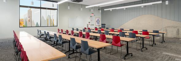 Training room with wood tables, red and gray chairs, large window, and textured gray walls.