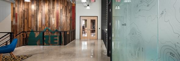Hallway with reclaimed wood wall, glass map design, polished floor, and REI logo near stairs.