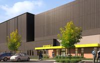 Rendering of a studio building with a sleek dark facade, yellow accents, parking lot, and green landscaping.