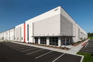 Corner of warehouse facility with a clean white facade, red accents, and spacious parking lot.