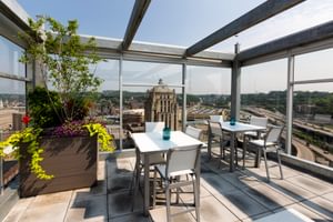 Rooftop patio with tables, chairs, greenery, and scenic views of the city and historic architecture.