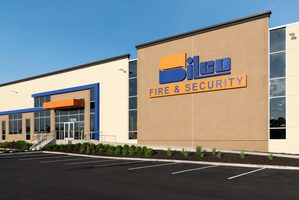 Office building with beige brick, blue trim, orange accents, and glass windows. Silco Fire & Security logo is on front.