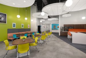 Bright breakroom with colorful chairs, green accent wall, orange backsplash, and modern lighting fixtures.