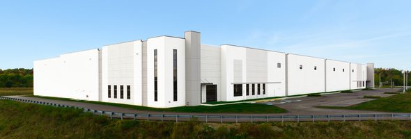 White industrial building with tall windows, gray accents, and green landscaping.
