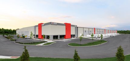 Wide view of building with beige and red exterior, parking lot, and surrounding greenery. Standard Textile logo is at top.