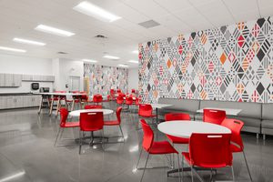Tenant cafeteria with red chairs, round tables, geometric patterned walls, and gray cabinetry.