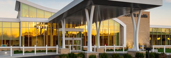 Close-up of exterior building entrance with glass facade, modern canopy, and warm sunset reflections.