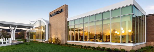 Exterior of building with glass windows, sunset reflections, and Vanderbilt Health logo at the top.